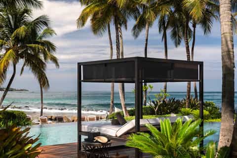 Beachfront cabana with black canopy overlooking palm trees and tropical ocean