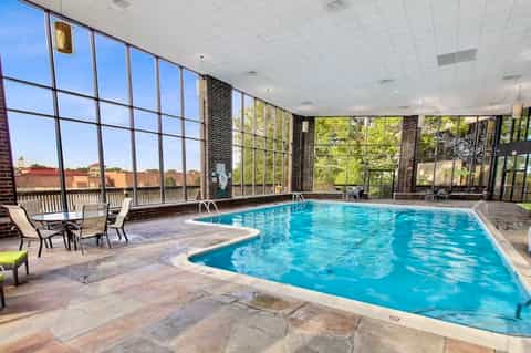 Indoor swimming pool with large windows overlooking grounds, lounge chairs visible