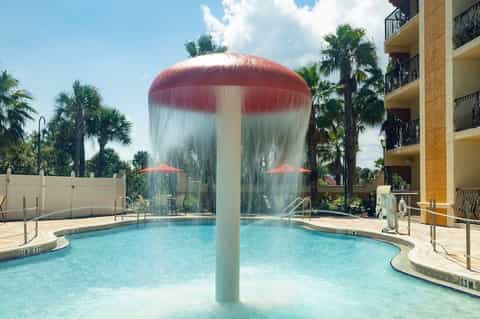 Resort pool with red mushroom-shaped water feature and palm trees surrounding deck