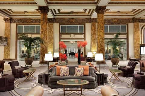 Luxurious hotel lobby with ornate columns, high ceilings, red floral arrangements, and elegant seating