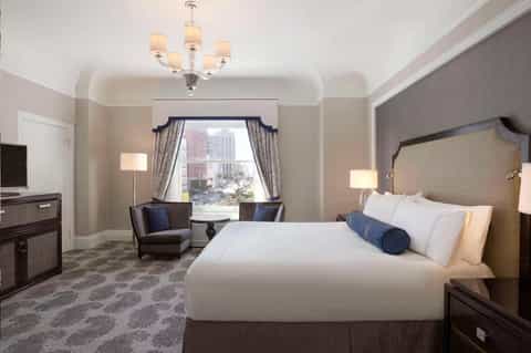 Luxury hotel suite with king bed, window seating area, chandelier, and city skyline views