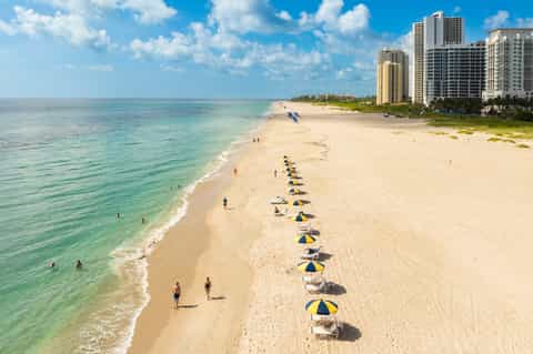 Sandy beach with blue umbrellas, turquoise ocean, and beachfront high-rise hotels