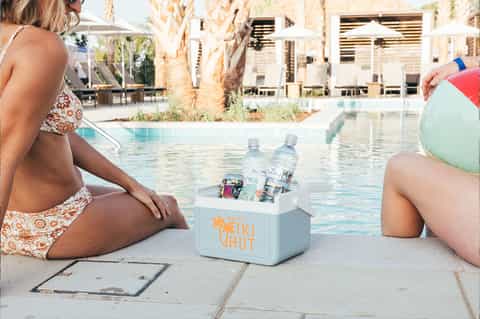 Two women poolside with branded cooler containing beverages and beach ball