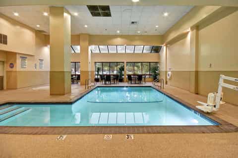 Indoor swimming pool with lane markers, beige walls, columns, and windows overlooking outdoor seating area