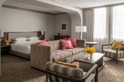 Luxury hotel suite with bed, gray sofa, colorful pillows, and modern furnishings