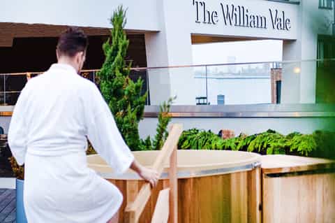 Man in white shirt leaning on wooden railing at The William Vale hotel with waterfront view