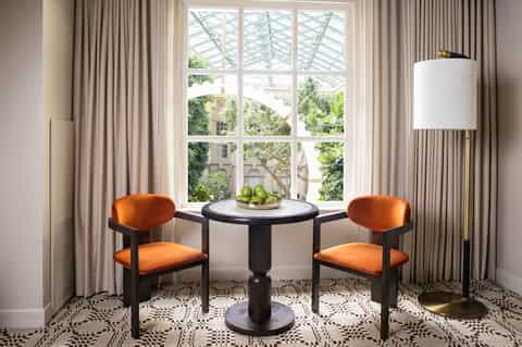 Elegant seating nook with orange velvet chairs, round black table, and large windows overlooking trees