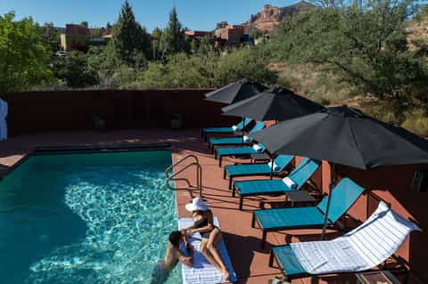 Resort swimming pool with turquoise water, black umbrellas, and desert mountain backdrop