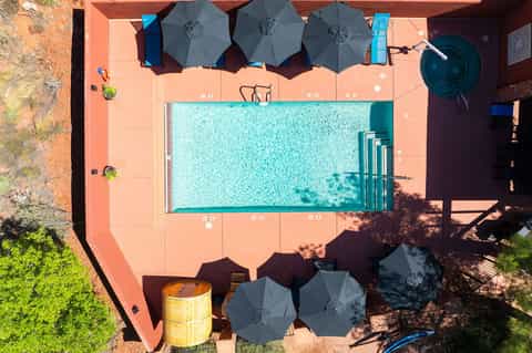 Aerial view of rectangular turquoise pool with umbrellas on terracotta patio surrounded by landscaping