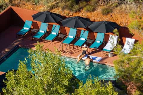 Resort pool nestled in red canyon landscape with turquoise loungers, black umbrellas, and desert vegetation