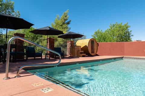 Outdoor pool area with playground slide, sauna barrel, umbrellas, and red wall