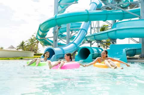 Three children playing in turquoise water with colorful inflatable rings in front of water slides