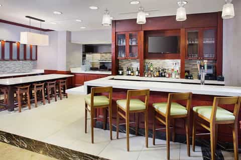 Contemporary bar and kitchen area with red wood cabinetry, pendant lighting, white countertops, and green bar stools