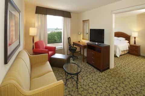 Hotel suite with living area, bedroom, desk, and window overlooking grounds
