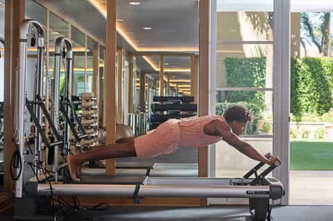 Man performing plank exercise on Pilates reformer machine in bright fitness studio with garden view