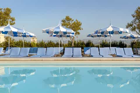 Resort pool with blue and white striped umbrellas, white lounge chairs, and mountain views in background