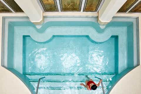 Overhead view of indoor pool with decorative tile mosaic and swimmer in red doing backstroke