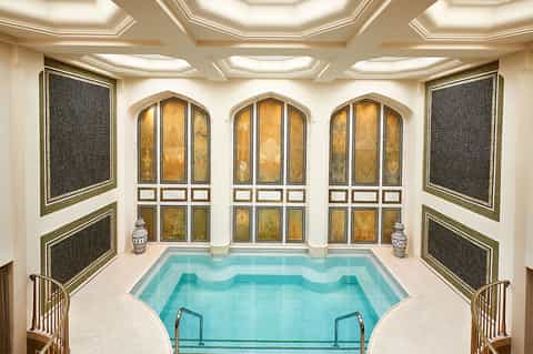 Luxurious indoor swimming pool with gold decorative doors, arched windows, and spa-like ambiance