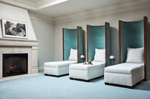 Luxury spa room with three white beds, teal headboards, fireplace, and elegant furnishings