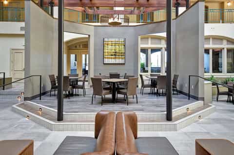 Modern hotel atrium with round dining tables, upper balconies, and natural lighting