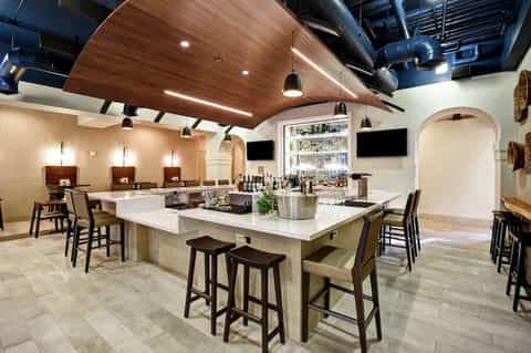 Modern bar and lounge with wooden ceiling, white marble countertop, pendant lighting, and dark wood furnishings
