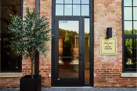 Spa entrance with brick facade, black door, and signage for The Spa at Rivet House