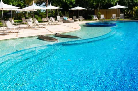 Resort pool with turquoise water, white umbrellas, lounge chairs, and manicured lawn areas