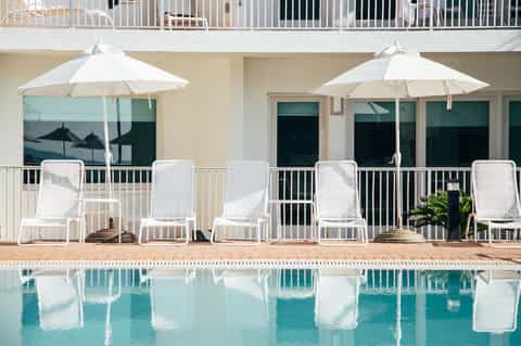 Poolside lounge area with white chairs, umbrellas, and reflecting water at modern resort