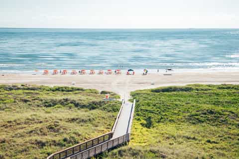 Beach access with wooden boardwalk, sandy shore, striped umbrellas, and ocean horizon