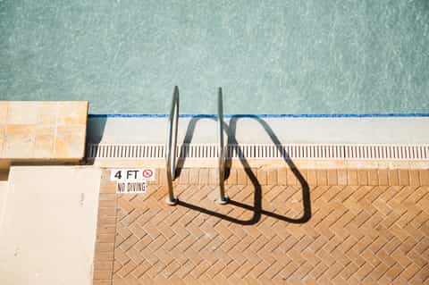 Pool edge with ladder and no diving sign at shallow end
