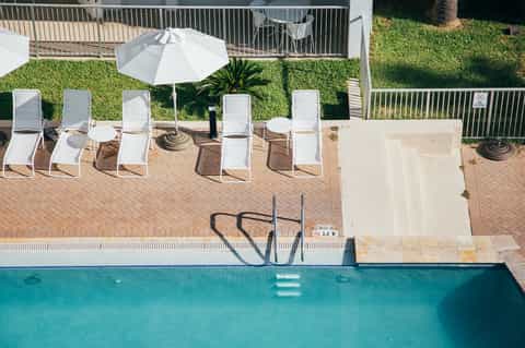 Outdoor pool deck with white lounge chairs, white umbrella, green lawn, and metal railings