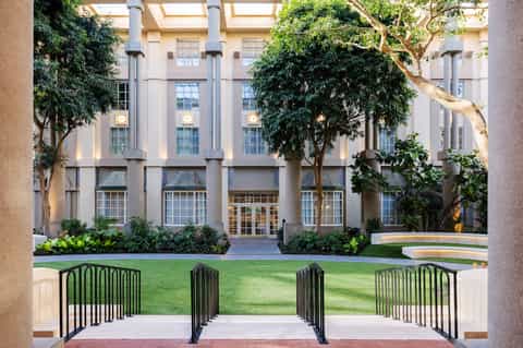 Modern courtyard with manicured lawn, large trees, contemporary building facade, and metal railings