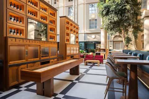 Upscale hotel lounge with wooden wine display cabinets, modern furniture, and natural light from high ceilings