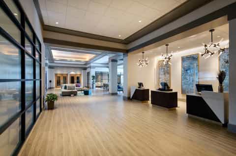 Modern hotel lobby with wooden flooring, reception desks, pendant lighting, and seating area