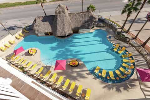 Resort pool complex with turquoise water, thatched-roof cabana, lounge chairs, and palm trees