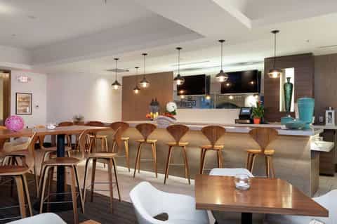 Modern hotel lobby bar with wooden mid-century chairs, pendant lighting, and stone countertop with decorative accents