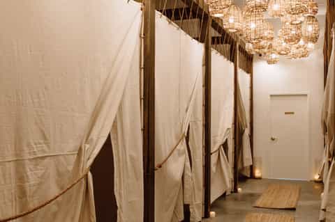 Spa relaxation room with draped fabric partitions, wooden flooring, and woven pendant lighting