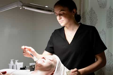 Skincare professional applying facial treatment to client under bright lamp