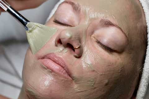 Spa treatment close-up showing facial mask application with brush on woman's face