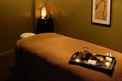 Spa massage room with olive walls, massage bed, dim lighting, and aromatherapy setup