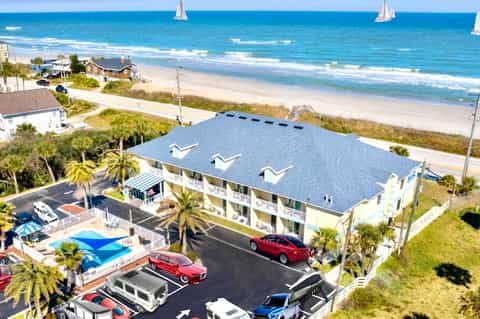 Beachfront residential building with blue roof, parking lot, and sailboats on ocean