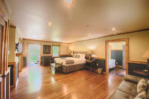 Spacious hotel suite with king bed, fireplace, wooden floors, and sliding glass doors to outdoor balcony