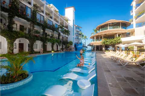 Resort pool with lounge chairs, tiki-style umbrellas, and white architecture