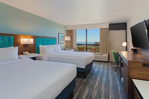 Beachfront hotel room with two queen beds, ocean view from balcony, and flat-screen TV