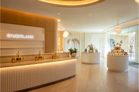 Upscale Guerlain beauty boutique interior with curved cream-colored counter, golden bottles, and modern luxury spa design