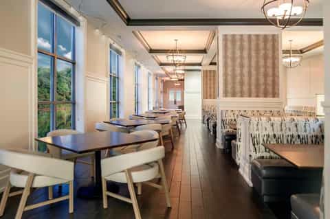 Elegant dining room with long tables, wooden chairs, pendant lights, and large windows overlooking greenery