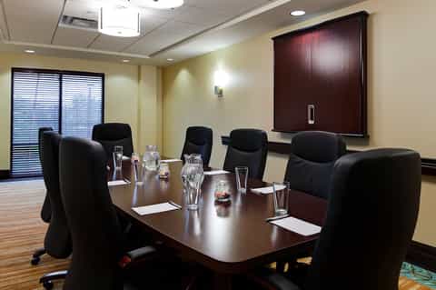 Hotel conference room with long dark wood table, black chairs, and presentation screen