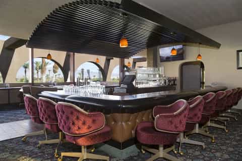 Upscale bar lounge with burgundy velvet chairs, black curved bar counter, and panoramic desert views