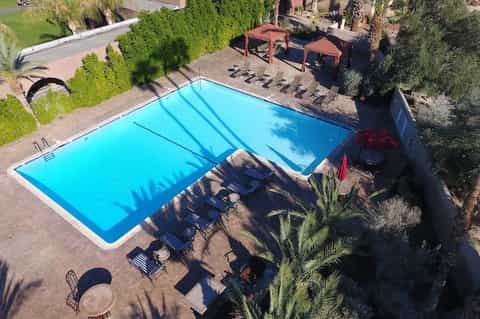 Aerial view of rectangular blue pool with black lounge chairs and palm trees