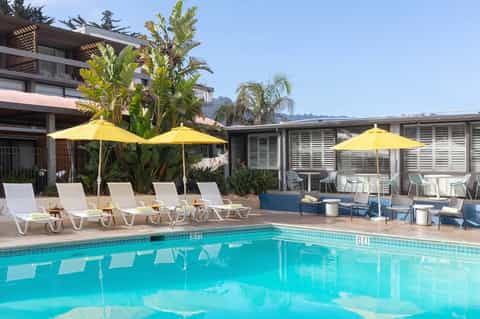 Resort pool area with yellow umbrellas, lounge chairs, and mountain backdrop under clear sky